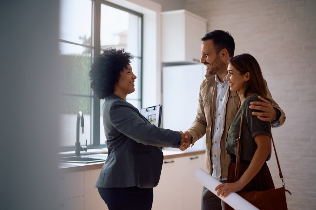 Happy real estate agent shaking hands with potential new home buyers.