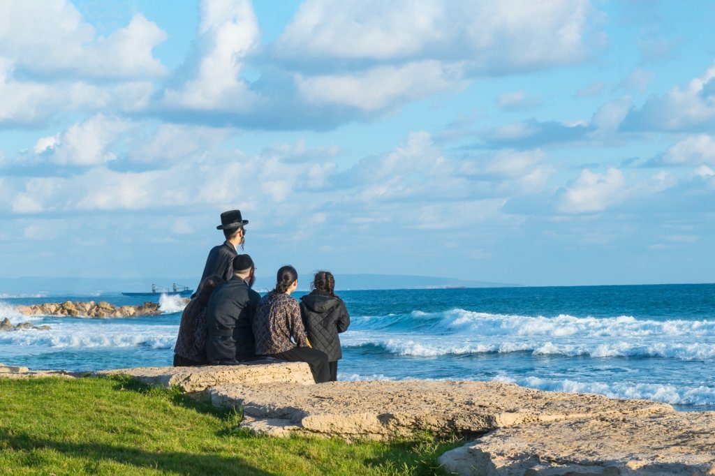 Religious Jew family sitting on the coast of Mediterranean sea in Israel and watching the waves.