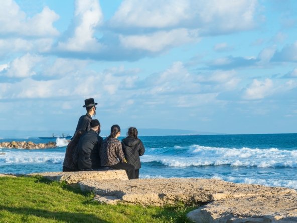 Religious Jew family sitting on the coast of Mediterranean sea in Israel and watching the waves.