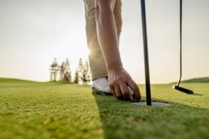 Golfer putting golf ball on golf course, lens flare on evening sun.Professional golf course at sunse