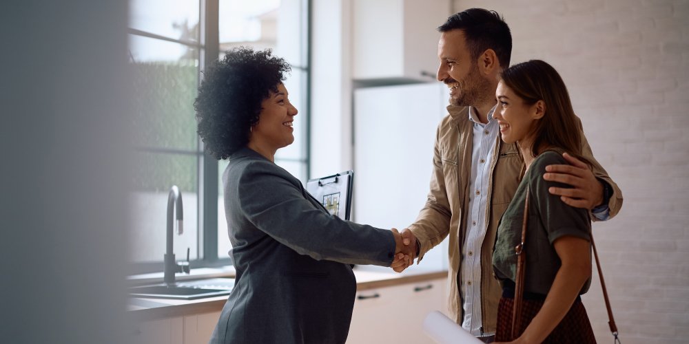 Happy real estate agent shaking hands with potential new home buyers.